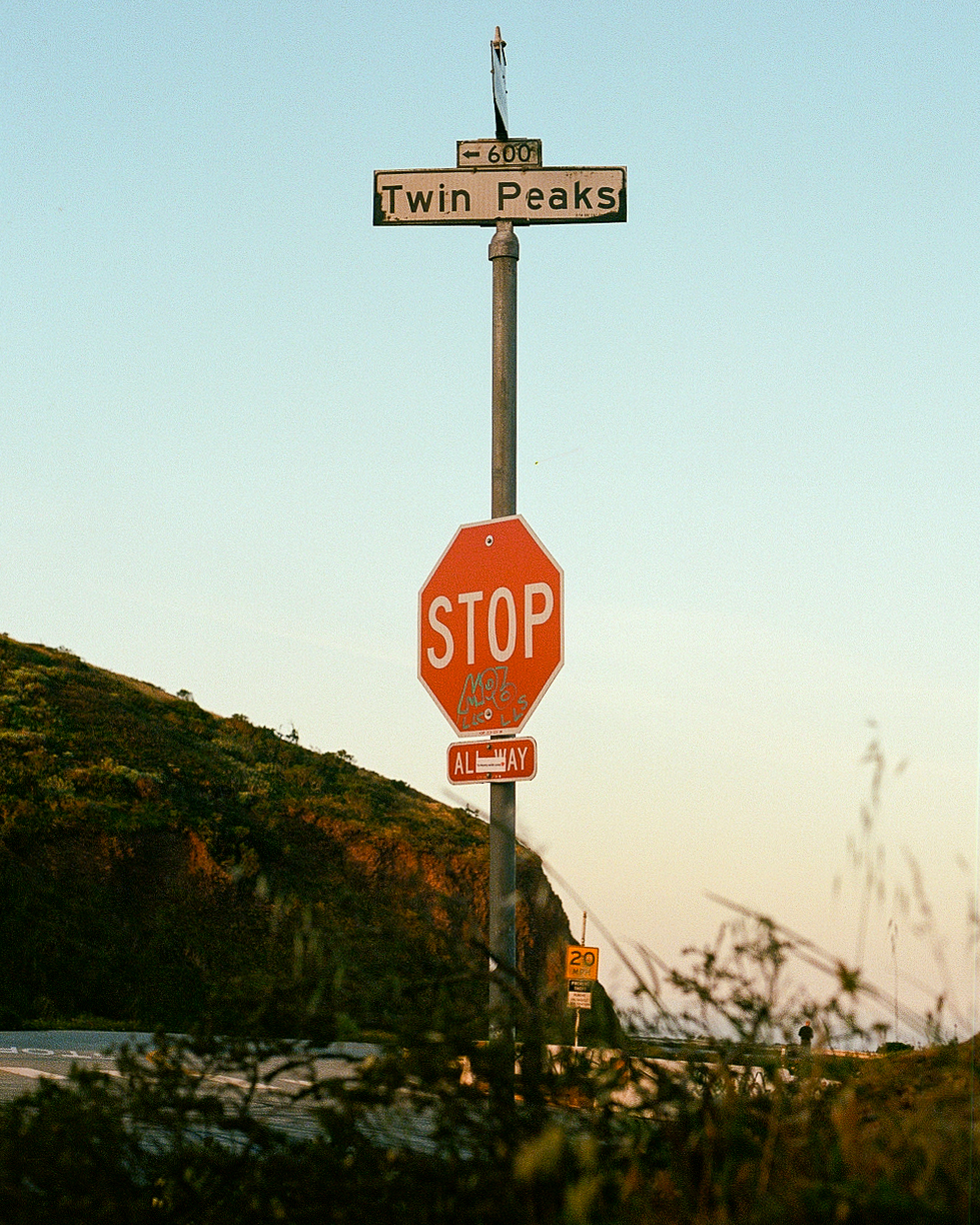Twin Peaks street sign with stop sign at sunset against hillside