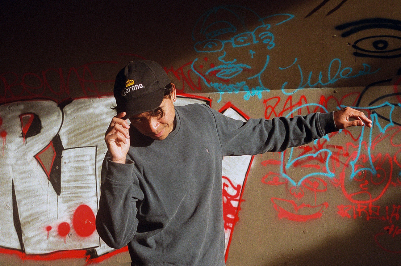 Person in Corona cap and gray sweatshirt against graffiti wall