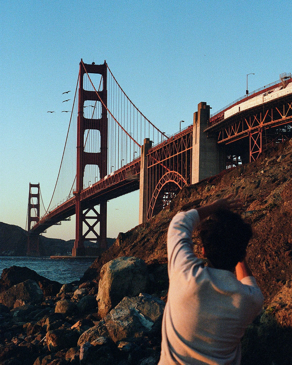 Person looking at Golden Gate Bridge from rocky shoreline at sunset