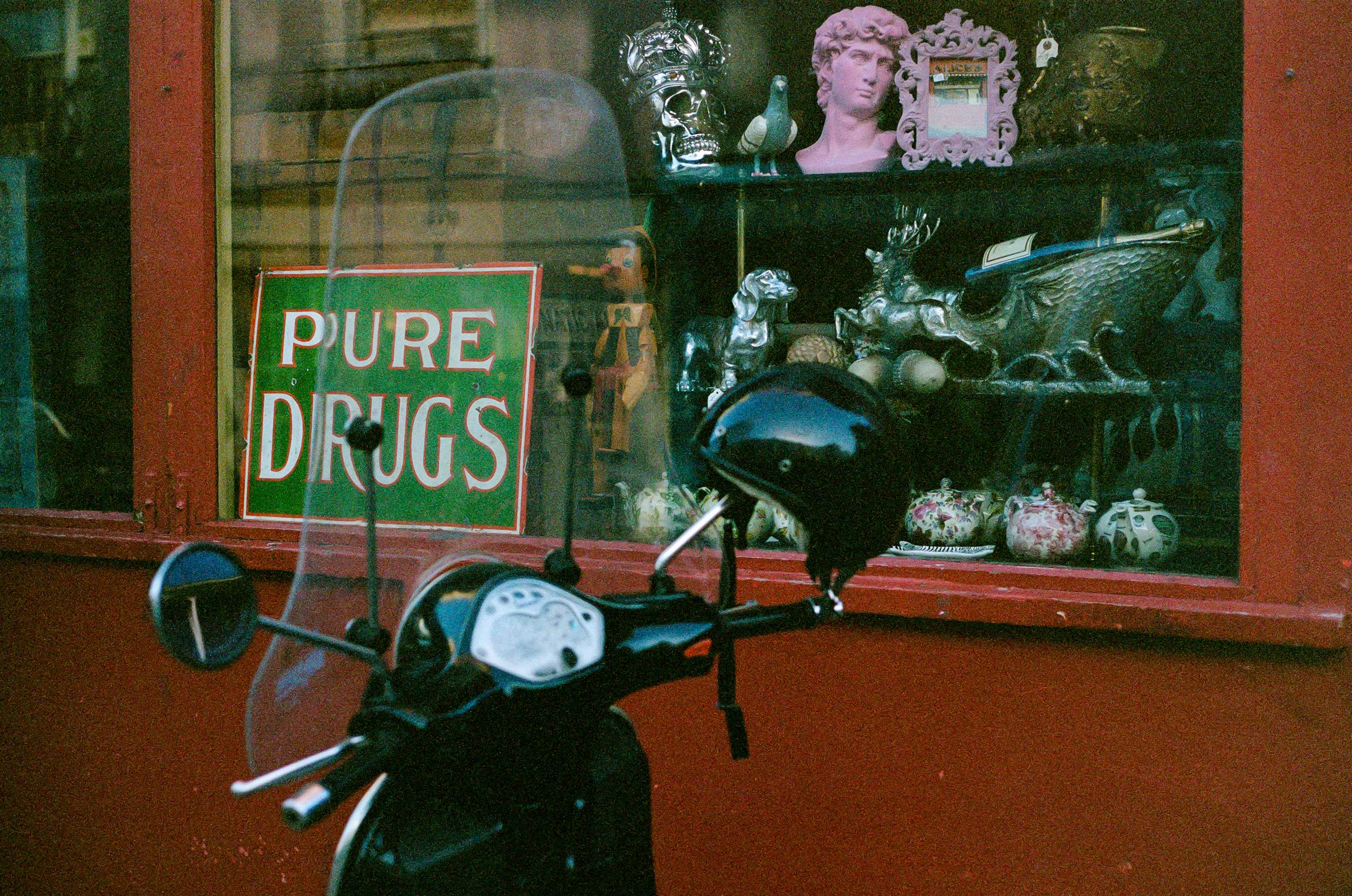 Scooter parked in front of vintage shop window with PURE DRUGS sign