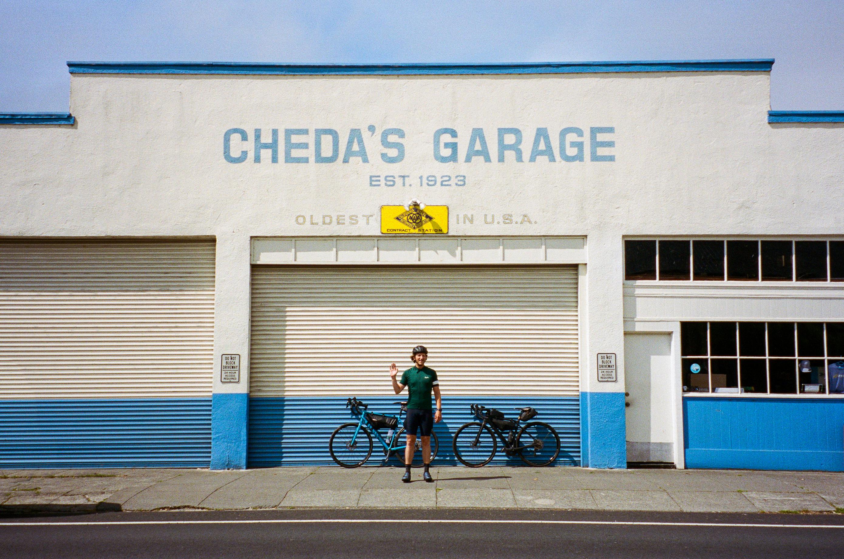 Cyclist standing in front of Cheda's Garage with blue and white building facade
